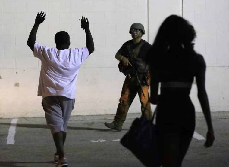 Image: A man raises his hands as he walks near a law enforcement officer