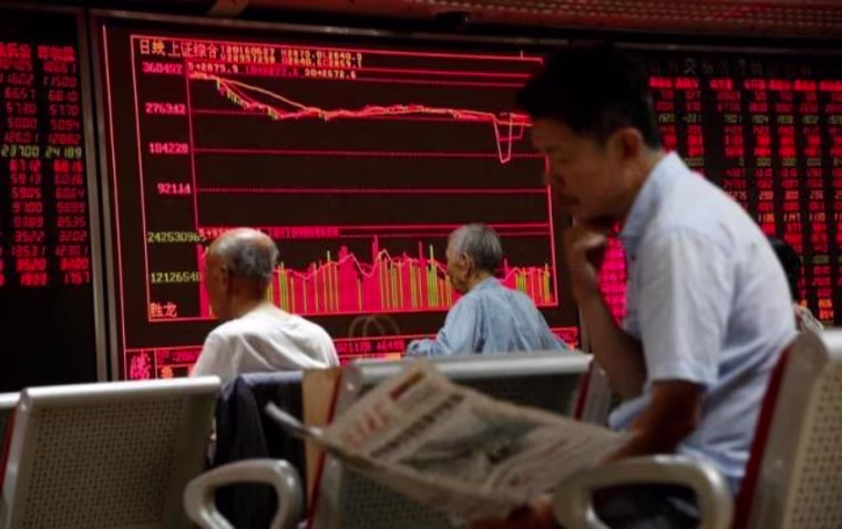 A man reads a newspaper in front of an electronic board at a brokerage house in Beijing