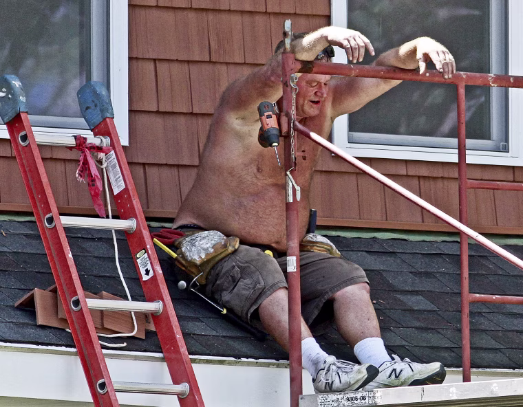 Jim Darnell, of Darnell Home Improvement, waits in the shade as a co-worker cuts another piece of siding for a home improvement job on July 21, 2016, in Quincy, Ill. Outdoor workers had to take more breaks than usual with the temperature in the upper 90's and the heat index in the 100s.