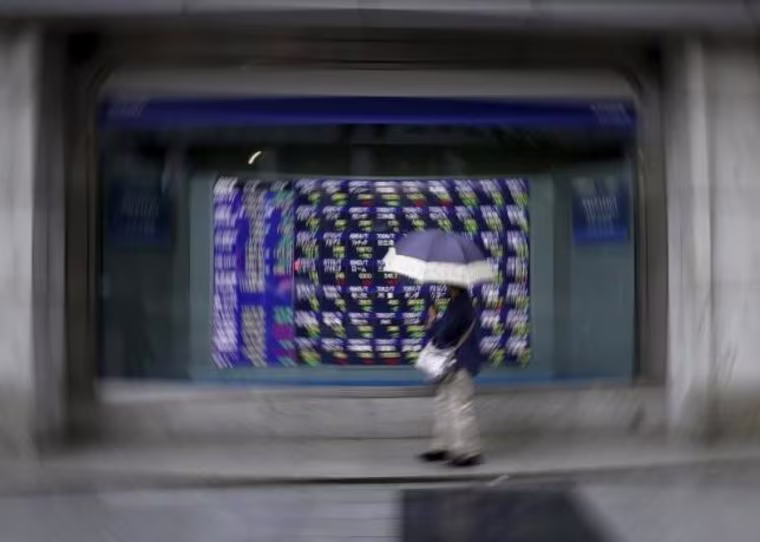 A woman holding an umbrella looks at an electronic stock quotation board outside a brokerage in Tokyo
