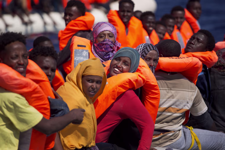 Image: Migrant women smile on board of a dinghy as they sail in the Mediterranean sea