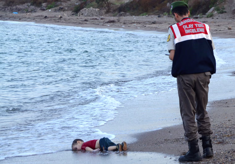 Image: A Turkish police officer stands next to a migrant child's dead body