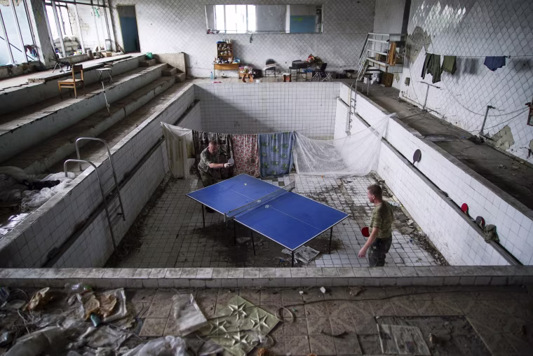 Image: Ukrainian soldiers play table tennis at a damaged swimming pool in the village of Marinka