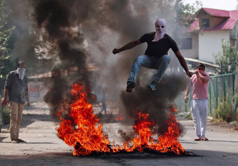 Image: A man in a balaclava jumps over burning debris during a protest against the recent killings in Kashmir, in Srinagar