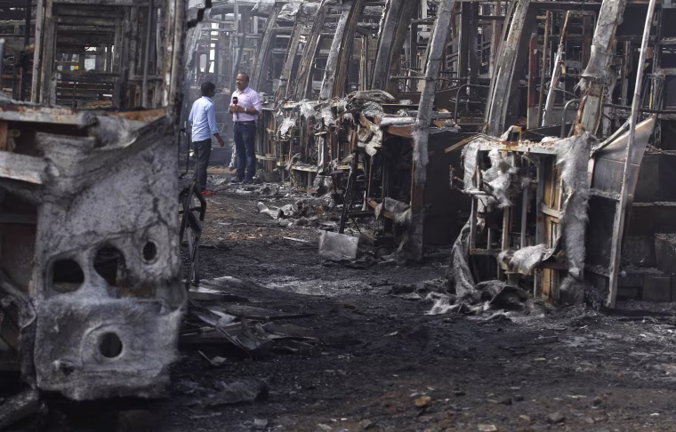 Image: A television journalist reports amidst the charred remains of passenger buses