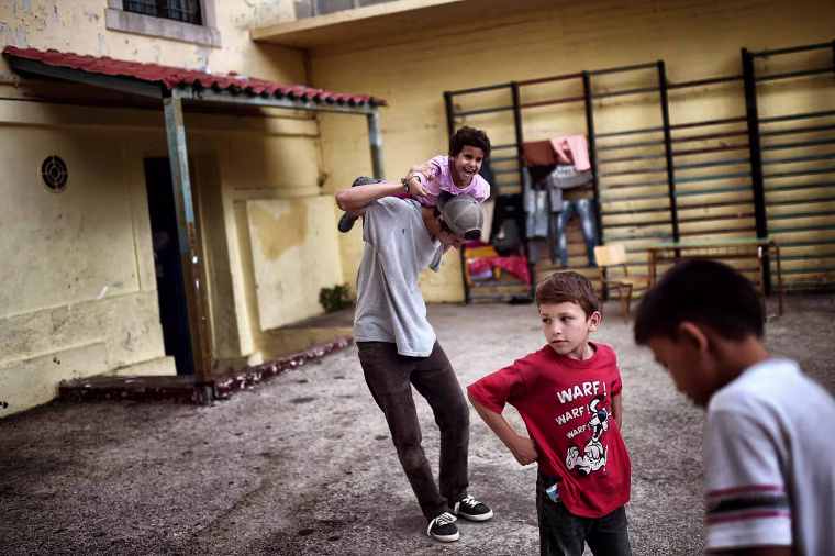 Image: Children play at the yard of an abandoned school used by volunteers for hosting families of refugeees
