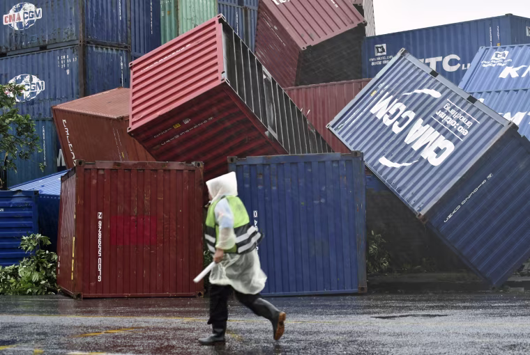 Image: A man walks past downed shipping containers at the Kaohsiung Harbor