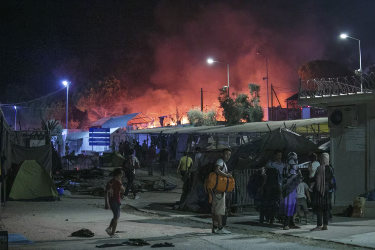 Image: Migrants hold their belonging as a large fire burns inside the Moria refugee camp