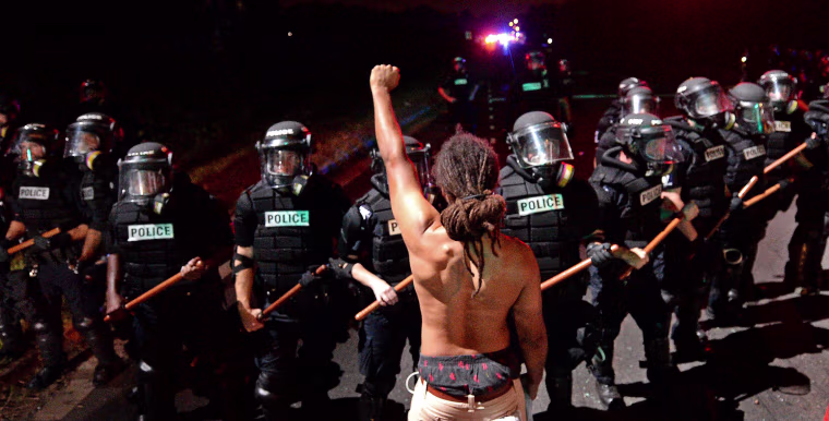 Image: A protester stands with his arm extended and fist clenched in front of a line of police officers in Charlotte