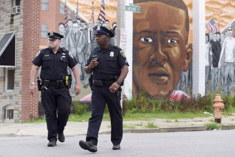 Image: Baltimore police walk near a mural depicting Freddie Gray