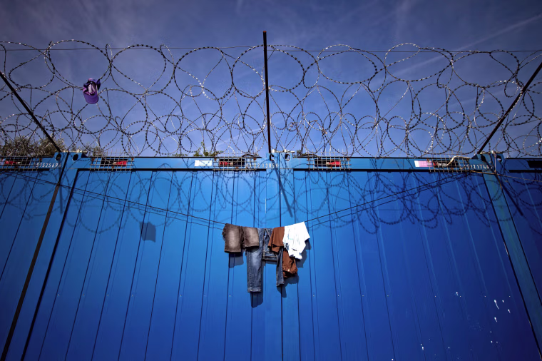 Image: Clothes hang on the barbed wires at a makeshift refugee and migrants camp