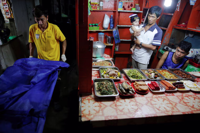 Image: A food vendor holds a baby as funeral workers carry the body of one of two men killed inside a slum in port area on Manila
