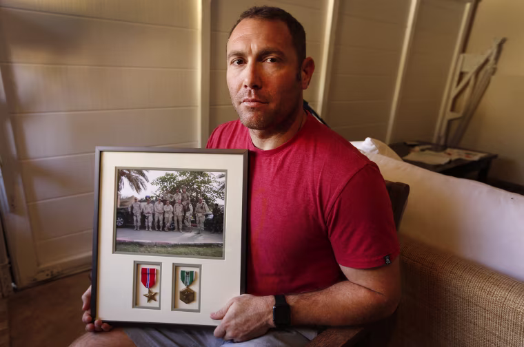 Robert D'Andrea, an Iraq war veteran who served with the U.S. Army and the California National Guard, holds a frame with a photo of his team on his first deployment to Iraq in his home in Los Angeles.