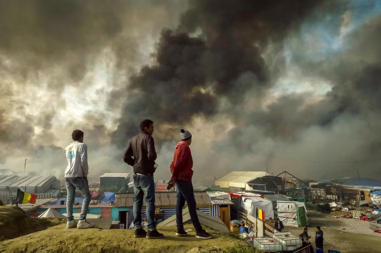 Image: Migrants stand on a hill overlooking the \"Jungle\" migrant camp in Calais