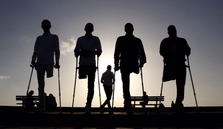 Image: Four Palestinian friends who were injured during conflicts walk by the sea at Gaza's small fishing harbor