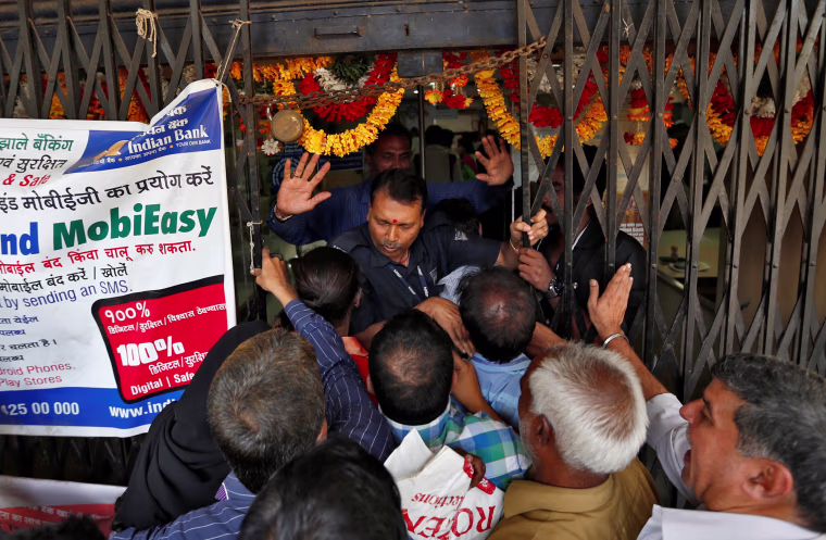 Image: A security guard tries to close the gate as as people try to enter a bank in Mumbai