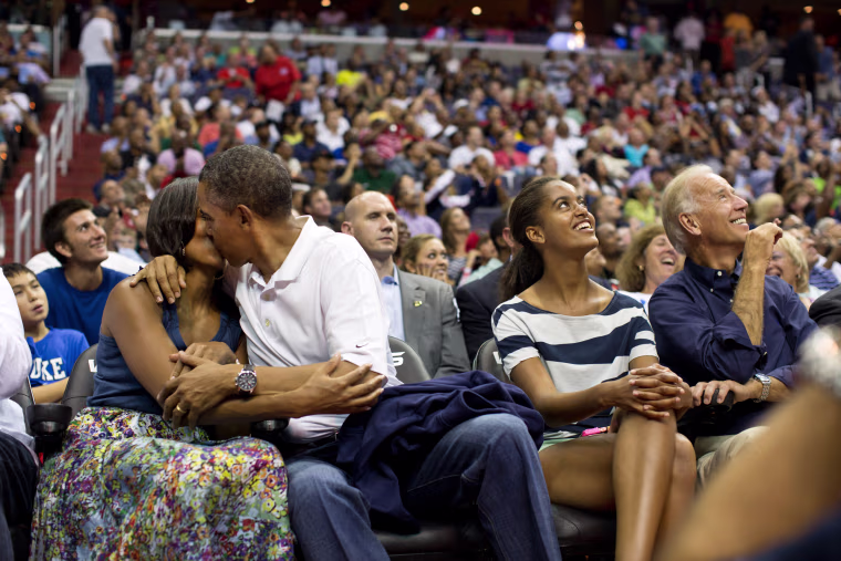 President Barack Obama kisses First Lady Michelle Obama for the \"Kiss Cam\" while attending the U.S. Men's Olympic basketball team's game against Brazil at the Verizon Center in Washington, D.C., July 16, 2012. Vice President Joe Biden and Malia Obama look up at the jumbotron.