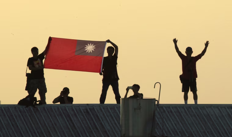 Locals on a warehouse rooftop display the national flag while watching Taiwan fighter jets practice emergency landing drills on a closed section of highway during the annual Han Kuang military exercises in 2014, in Chiayi, central Taiwan.
