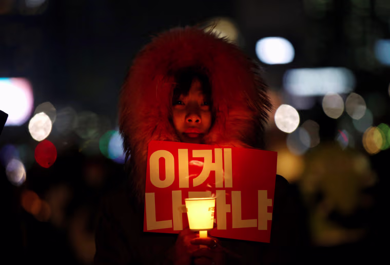 Image: A woman holds a candle light and a slogan at a protest calling South Korean President Park Geun-hye to step down in Seoul