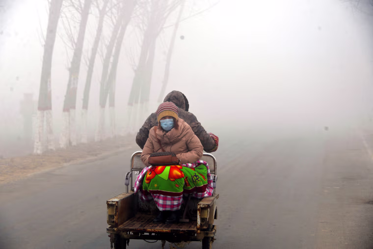 Image: A woman sits on the back of a motorcycle in smog during a polluted day in Liaocheng