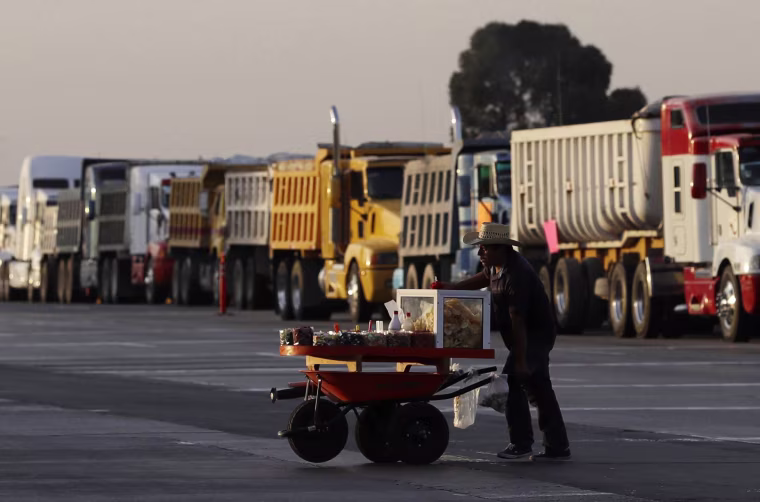 Image: A snack vendor takes advantage of a break in traffic to push his cart across a highway, where dozens of truck drivers angry over an increase in gas prices had parked their vehicles, put up signs, and were waved motorists through toll booths without