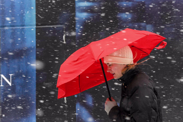 Image: A woman walks with a red umbrella during a snow storm in New York City