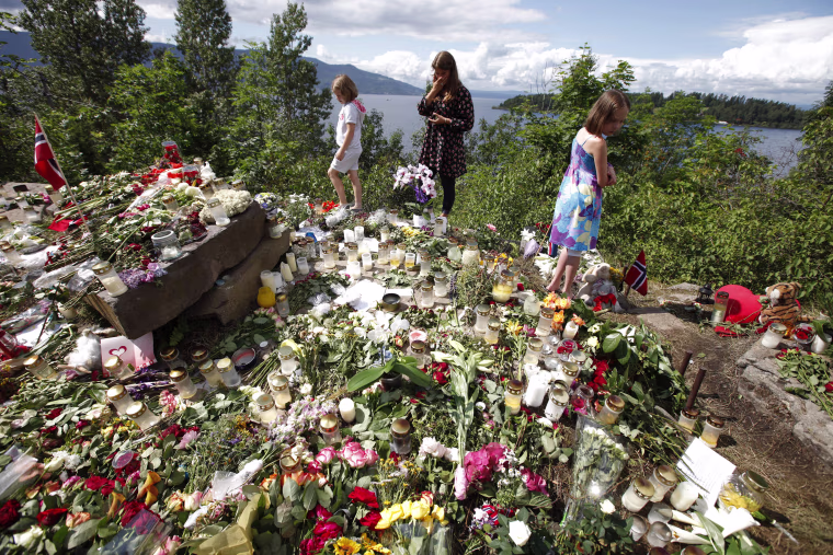 Image: Children stand at a temporary memorial site on the shore in front of Utoeya island