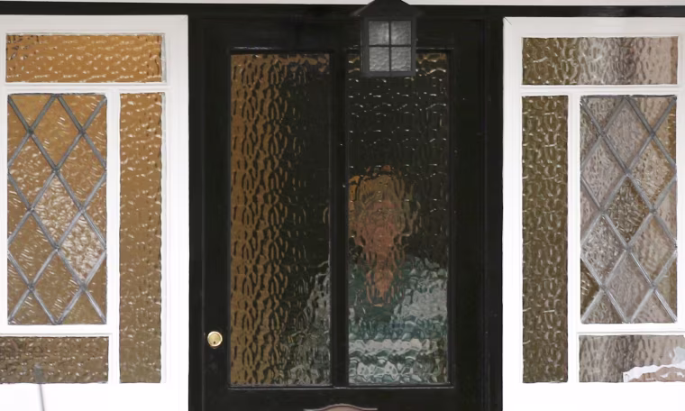 Image: A person stands behind textured glass at an address which has been linked by local media to former British intelligence officer Christopher Steele, who has been named as the author of an intelligence dossier on President-elect Donald Trump.