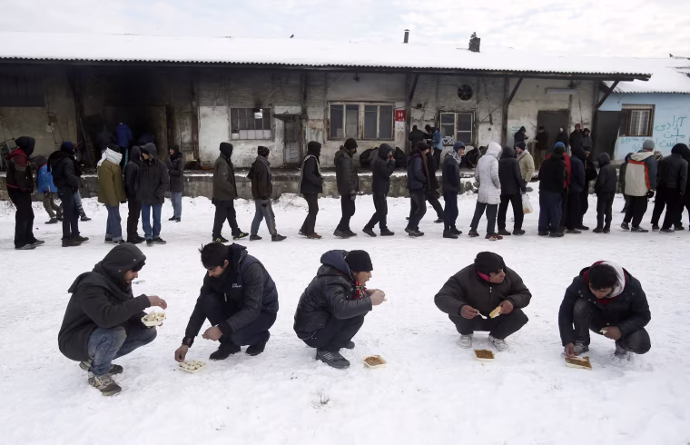 Image: Five migrants squat in the snow as they eat a warm meal distributed by aid groups as others queue for their portion outside a crumbling warehouse that has served as a makeshift shelter in Belgrade, Serbia, Jan. 12.