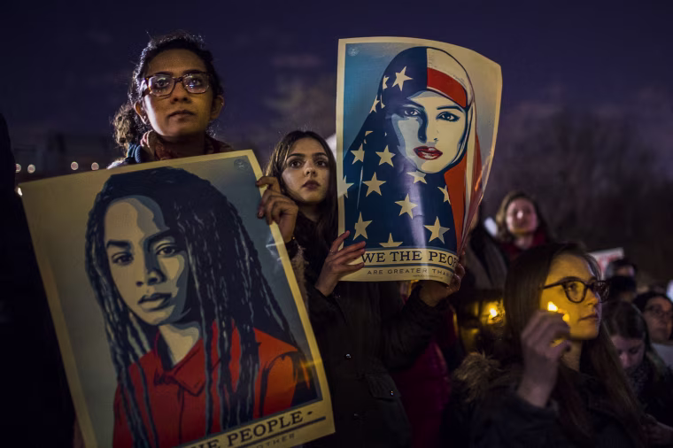 Image: Protesters listen to an speaker as the hold signs during a rally against President Donald Trump.