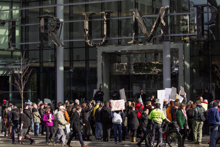 Image: Protesters hold signs outside of the Trump International Hotel and Tower during its grand opening in Vancouver