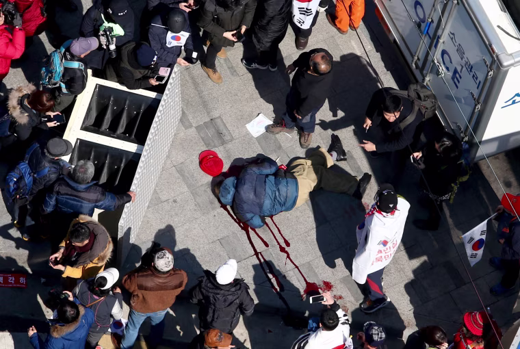 Image: An unidentified supporter of the impeached president lies on the ground in a pool of blood as protesters attempted to pass a barricade set up by the police, preventing access to the Constitutional Court following the court's ruling.