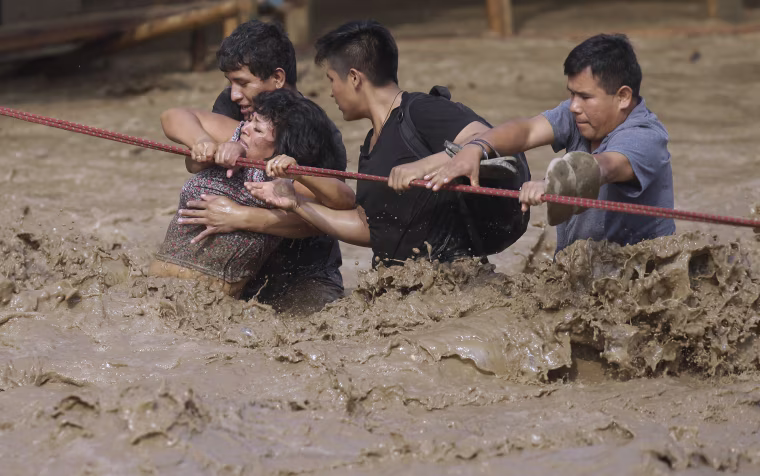 Image: A group of people, stranded in flood waters, hold onto a rope as they walk to safety in Lima, March 17.