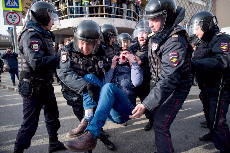 Image: Riot police officers detain a protester.