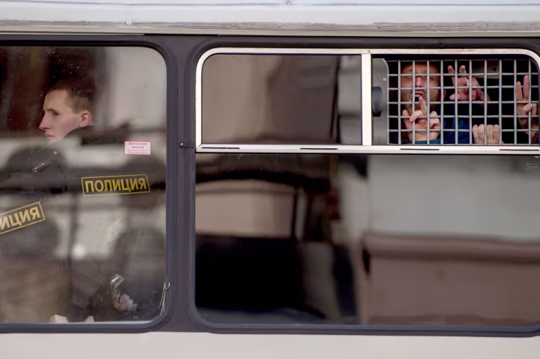 Image: Protesters gesture from a police bus after being detained.