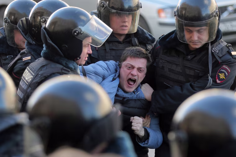 Image: Russian riot policemen detain one of dozens of demonstrators.