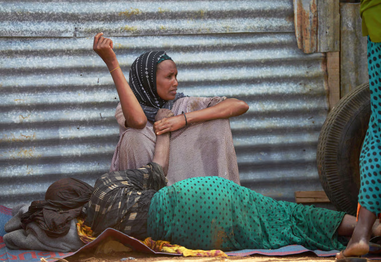 Image: An elderly woman weakened by hunger lies on the ground as her daughter watches over her at the camp, March 15.