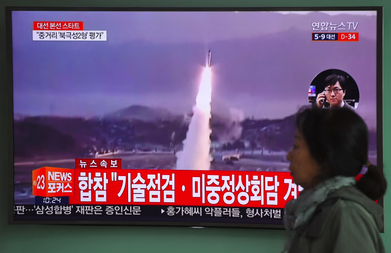 Image: A woman walks past a television screen showing file footage of a North Korean missile launch