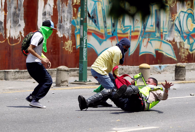 Image: Demonstrators grab a riot police officer during protests in Venezuela