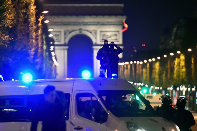 Image: Police look through binoculars as officers secure the area after a gunman opened fire on the Champs Elysees