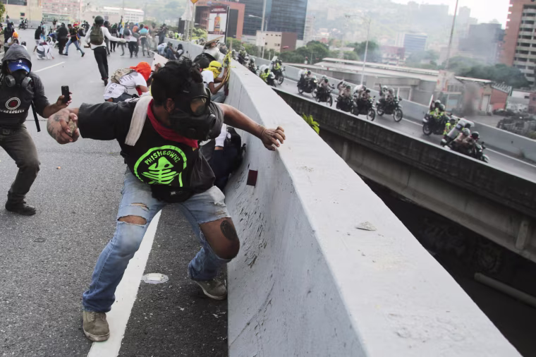 Image: Anti-government protesters throw stones from a highway overpass at a passing police patrol in Caracas