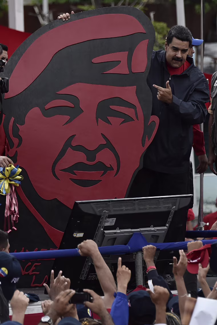 Image: President Nicolas Maduro stands next to a placard depicting late leader Hugo Chavez