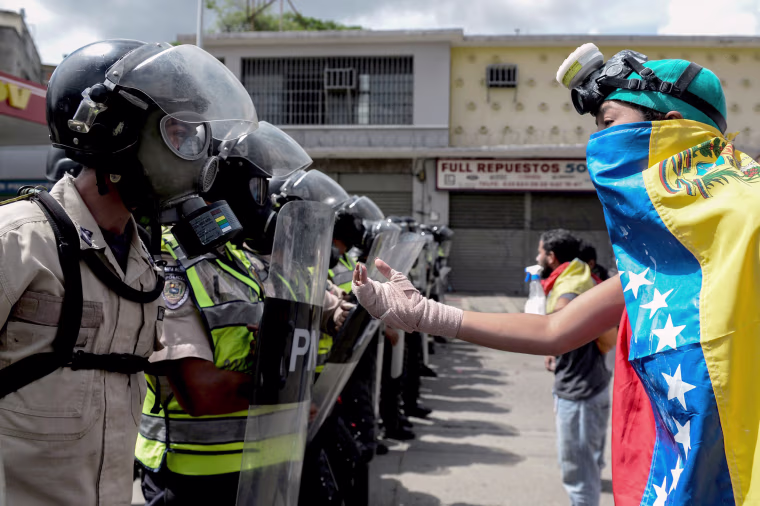 Image: A Venezuelan opposition activist faces police agents during a march against President Maduro, in Caracas on May 1, 2017.