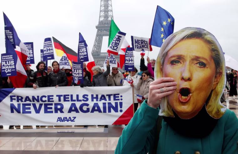 Image: A protester holds a Marine Le Pen mask near banner reading "France Tells Hate: Never Again"