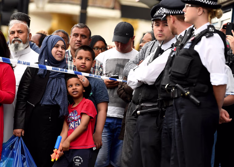 Image: A boy holds a water gun as police officers stand on duty inside a cordon in East Ham,where police are conducting a raid.