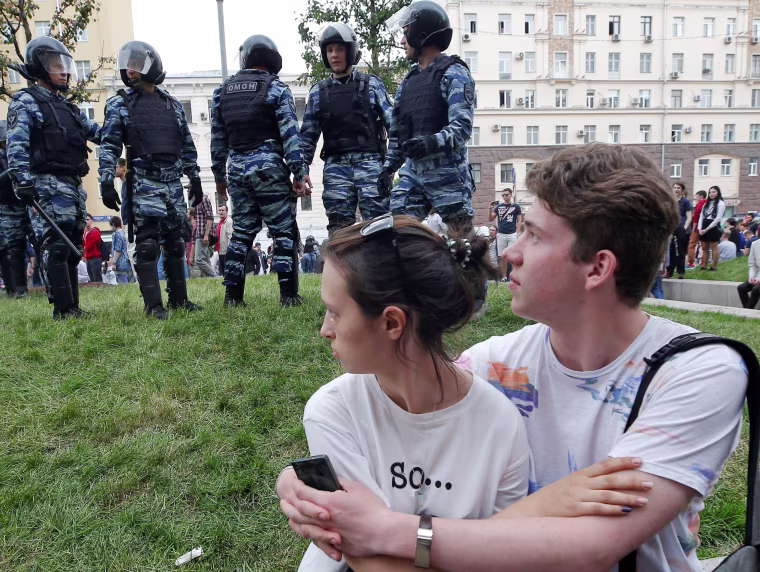 Image: A couple sits in front of riot police standing guard during an anti-corruption protest in central Moscow