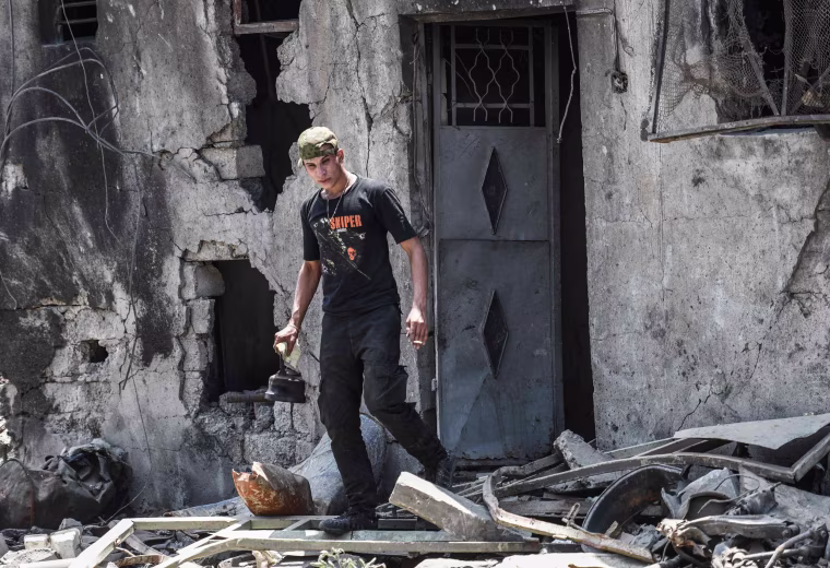 Image: A member of the Iraqi forces leaves a damaged building carrying a kettle
