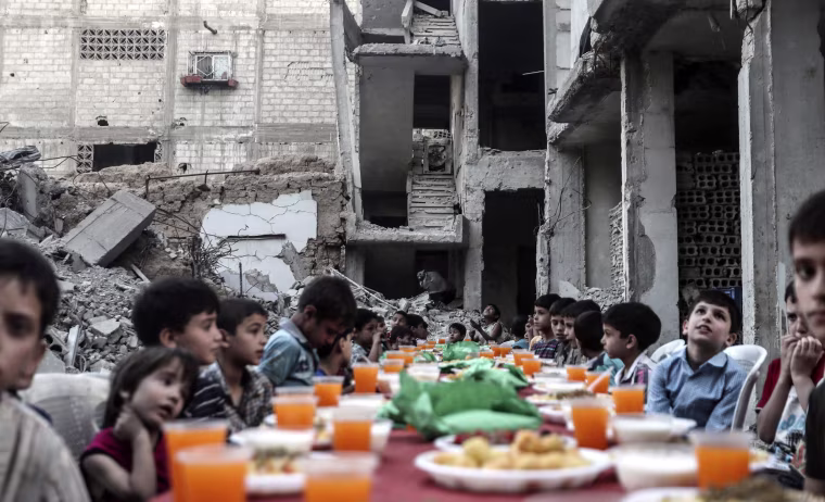 Image: Children sit at a table as they wait the evening meal at the end of daily Ramadan fast at sunset