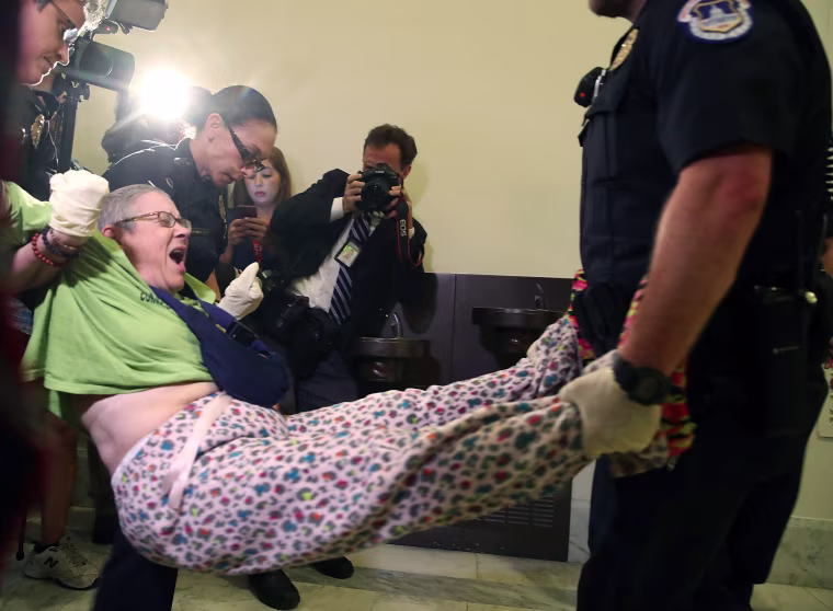 Image: U.S. Capitol Police remove a woman from a protest in front of the office of Senate Majority Leader Mitch McConnell