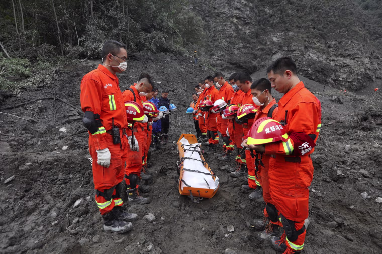 Image: Rescue workers stand in silent tribute before evacuating a body on June 25.